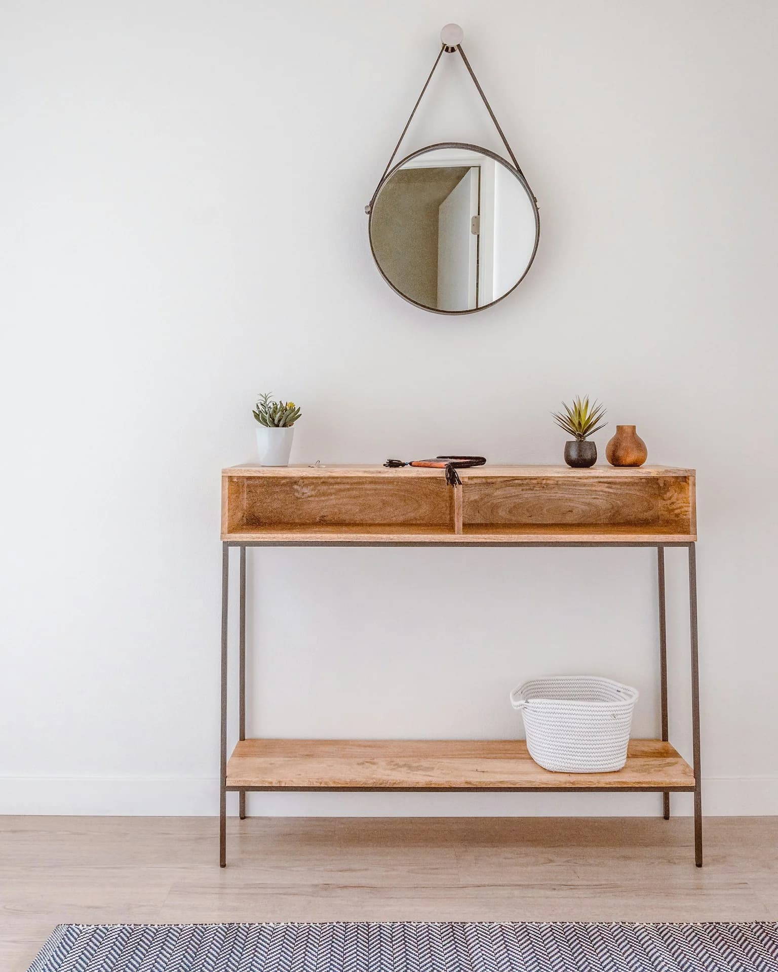 Consola de madera con plantas pequeñas, objetos decorativos y espejo redondo colgante