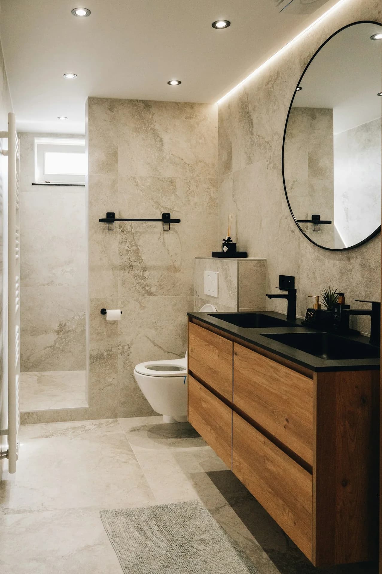Baño con mueble de madera, lavabo y grifería negros, espejo redondo y acabados de piedra